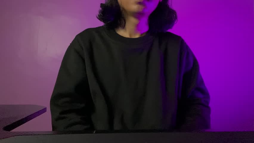 A man with long hair wear black crewneck show apologize gesture and pink light backround