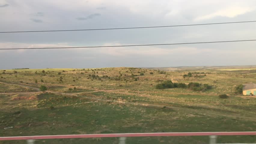 The area near railroad station and a sunlit meadow with a big shed shot from moving train in summer