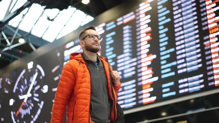 Passenger walk airport hall against FIDS. Male traveler check in trip. Guy fly away visit new city. Tourist man travel world. Happy person board plane. Train station arrival. Hipster hold backpack bag