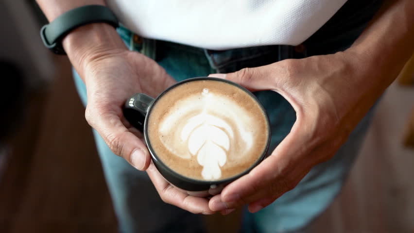 Hand of barista holding cup of latte art homemade coffee. top view 4K video