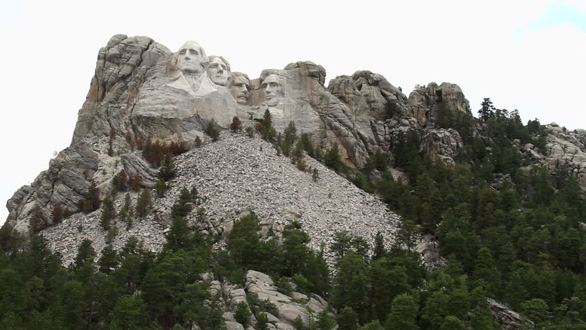 Mount Rushmore National Memorial in the Black Hills of South Dakota, on an Cloudy Day. Wide shot with fir trees on the surrounding mountain. The overcast sky adds a dramatic atmosphere.