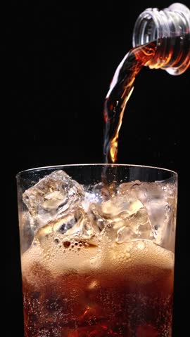 Closeup of pouring cola drink with ice cubes. Fizzing cola with ice in glass. Refreshing tasty cola drink.