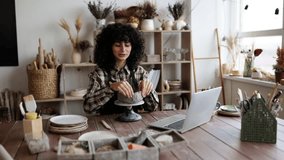 Female artist modeling clay in home pottery studio while on video call with laptop. Creative and artistic workspace. - Powered by Shutterstock - Get 15% off with code: PIKWIZARD15