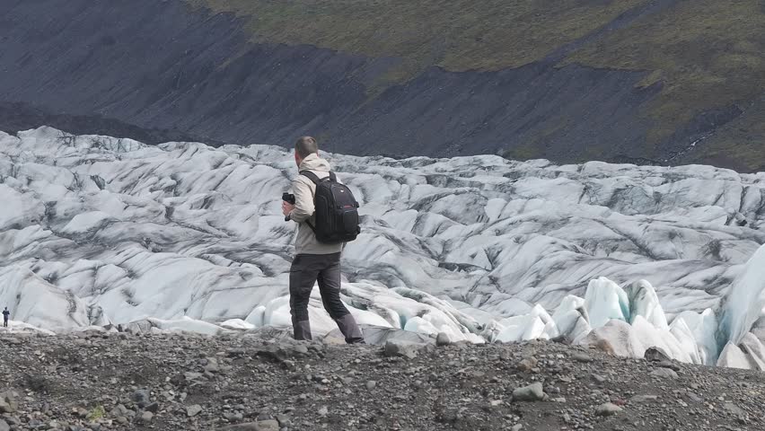Young man exploring Iceland glaciers. A Man Hiker looking at melting glacier - Melting of a iceberg and pouring water into the sea
