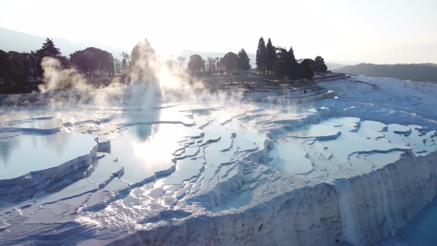 Steamy blue hot springs, mineral waters, forming travertine limestone mineral deposit formations. Pamukkale, Turkey (Türkiye) UNESCO World Heritage Site. Looking toward ancient Hierapolis city ruins