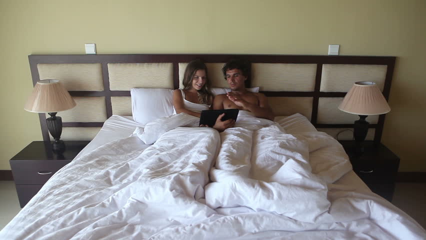 Happy beautiful pair relaxing with laptop in bed