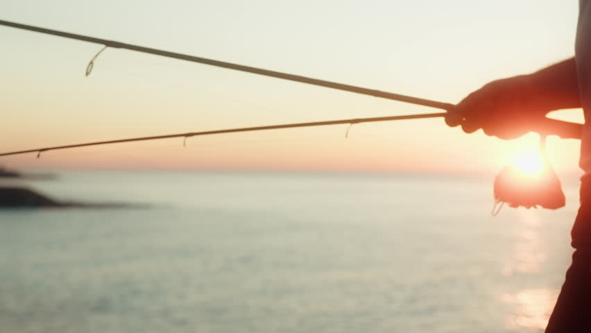 A fisherman standing on sea side and fishing against of sunset. Man setup the fishing rod