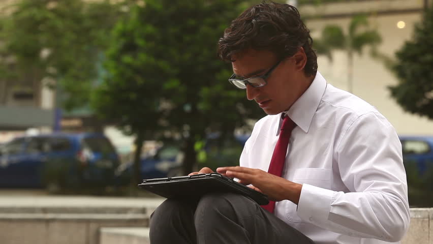 Serious businessman writes on a laptop outside
