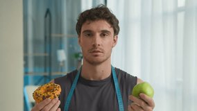 Caucasian man holding donut apple temptation choice weight sweet eating biting overeating calories junk food male thinking selection diet violation options unhealthy hunger smiling pleasure home guy - Powered by Shutterstock - Get 15% off with code: PIKWIZARD15