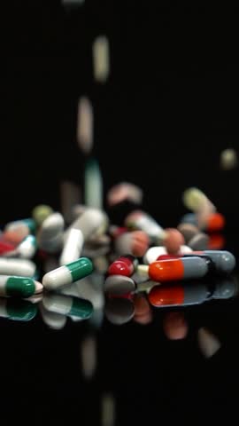 Pills Falling in Slow Motion on Black Surface - Medicine Background. Pharmaceutical Drugs on Black Background. Developing New Medicines. Drug Prices Keep Rising. Colorful Medicines. Part of a professional pharmaceutical production series. For matching clips and visual consistency, search for the unique series code: PHARMA-PROD-2026 or visit my dedicated collection: Pharmaceutical Manufacturing - PHARMA-PROD-2026