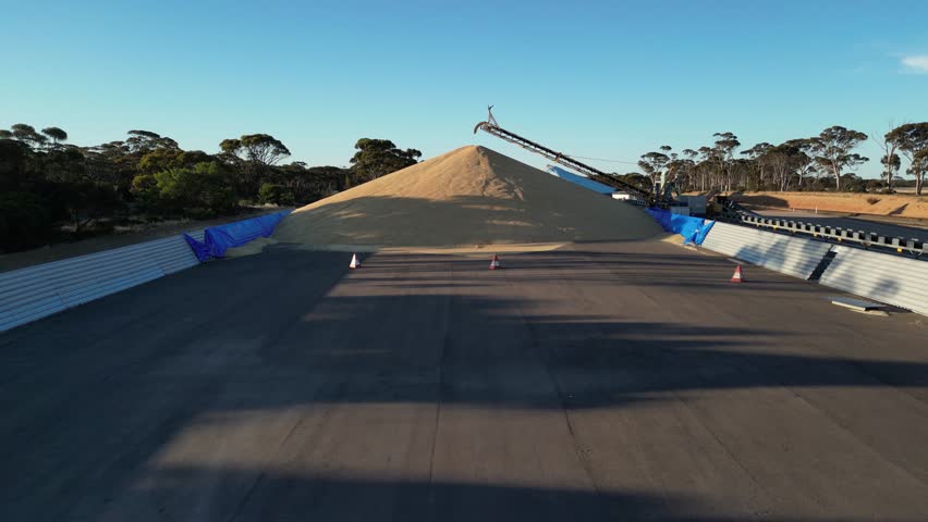 Aerial approaching shot of grain bulk transported by pipeline. Harvest wheat grains from field in season. Australian suburbia.