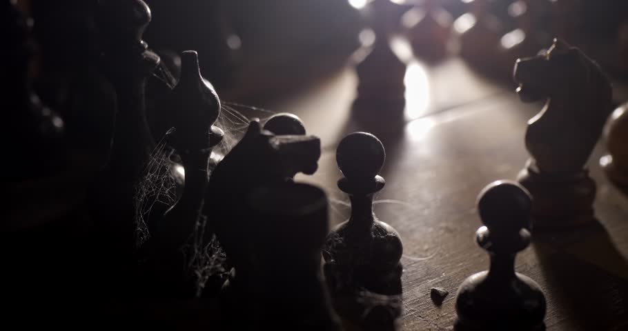 A chessboard with arranged pieces in dust and cobwebs rotates on a dark background in a ray of light. The Forgotten Party