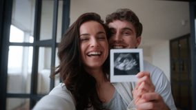 Webcam view influencer video record distant conference call vlog talking excited happy family couple Caucasian woman man guy male girl female parents showing USD picture pregnant baby ultrasound photo - Powered by Shutterstock - Get 15% off with code: PIKWIZARD15