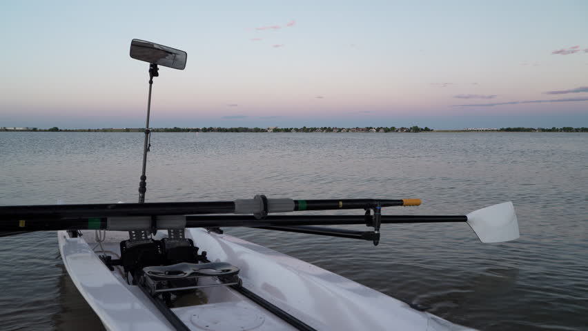Rowing shell with hatchet oars, sliding seat and rowing mirror is wobbling in waves at dusk on a shore of Boyd Lake, Colorado