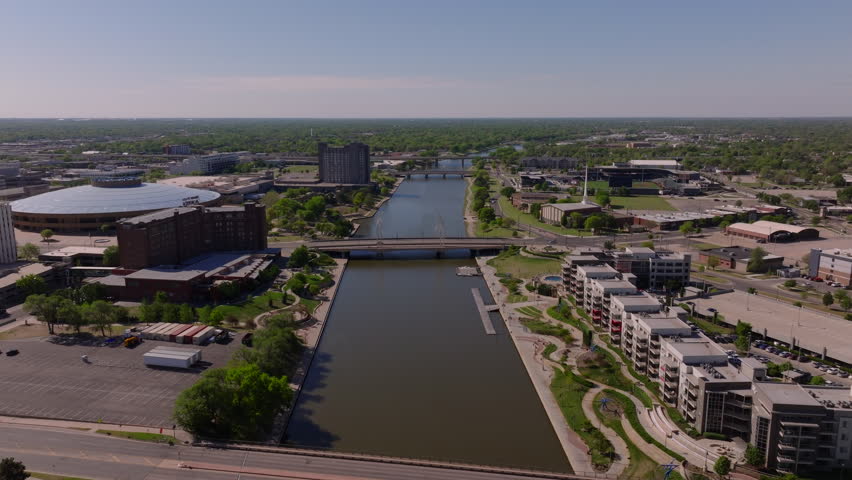 Vibrant cityscape of Wichita, kansas from above. Aerial footage captures modern buildings, green spaces, and Arkansas River under clear skies