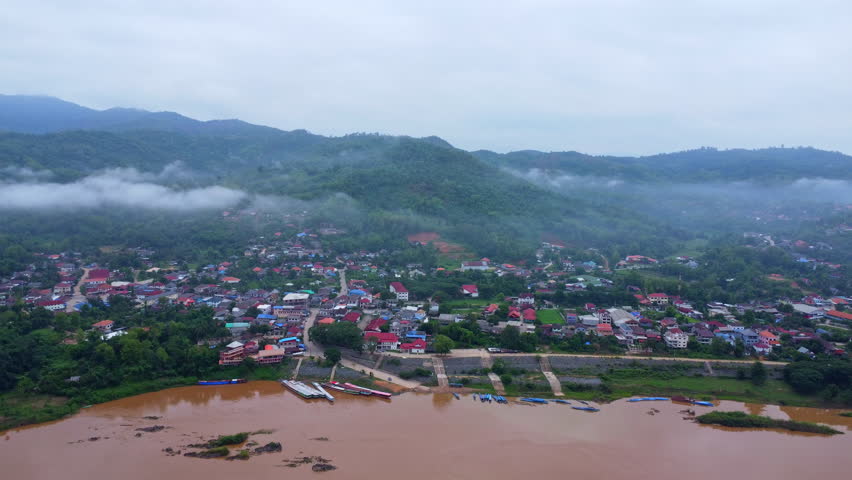 Aerial view of the mighty Mekong River winding from Chiang Khong, showing the vastness and beauty of the muddy waterway contrasting with the surrounding lush mountains and Laos villages.