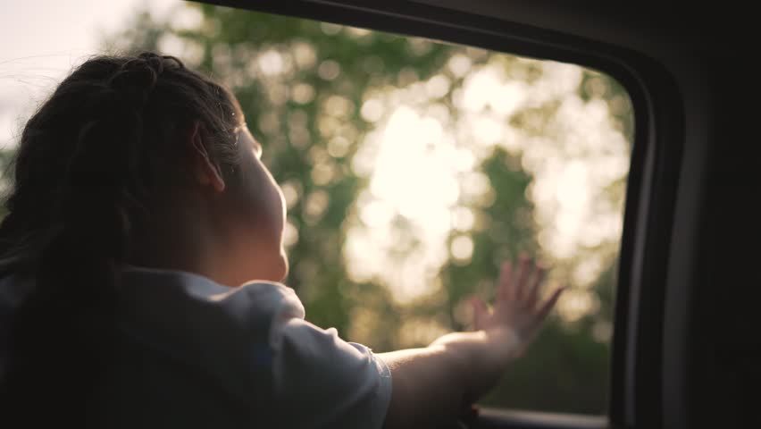 Child enjoying car travel with family. Happy child look out window. Sunset on girl face Family road trip moment. Child joyful travel experience. Window view during travel. Girl looking out car window