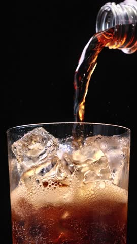 Closeup of pouring cola drink with ice cubes. Fizzing cola with ice in glass. Refreshing tasty cola drink, zoom in