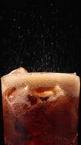 Closeup of pouring cola drink with ice cubes. Fizzing cola with ice in glass. Refreshing tasty cola drink, zoom in