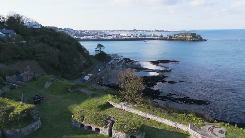Drone footage across the sea bathing pools and Havelet Bay Guernsey from Clarence Battery to Castle Cornet and St Peter Port on bright sunny day