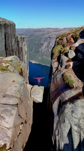 Asian women at the famous Kjeragbolten Majestic hanging stone, Kjerag, Norway, Lysefjordbrau in Norwegian fjord Lysefjord, Forsand municipality of Rogaland county, Norway in Summer