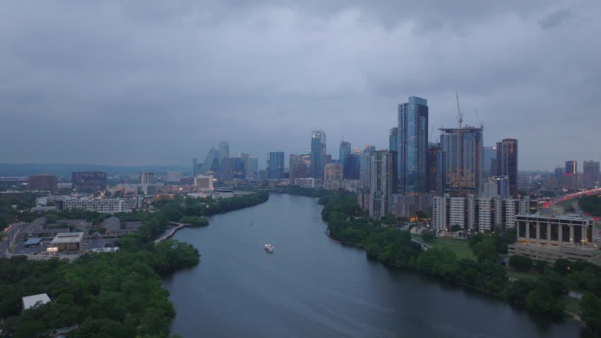Aerial view of Austin, Texas at dusk, featuring downtown skyline, high rise buildings, and scenic river with a boat. Cityscape and travel concepts