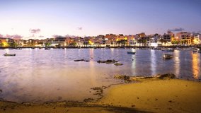 A time lapse of a nightfall on the bay of a small tourist town with a calm body of water and a few boats floating on it. The sky is a beautiful orange color, and the water is reflecting the sky.  - Powered by Shutterstock - Get 15% off with code: PIKWIZARD15