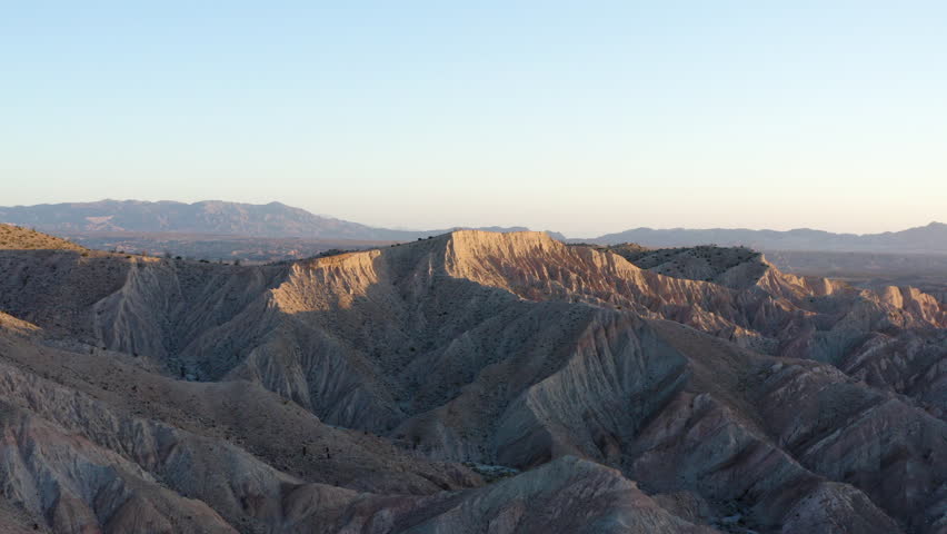 Aerial view of the rugged and dramatic Anza Borrego Badlands, showcasing the unique geological formations and textures of the eroded landscape under a clear sky during golden hour