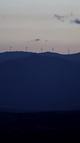 windmills turning on distant hills at sunset golden hour (electricity generation, green energy at dusk far away distance) greece, europe, mountains, vertical footage for mobile (turbines wind)