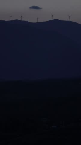 windmills turning on distant hills at sunset golden hour (electricity generation, green energy at dusk far away distance) greece, europe, mountains, vertical footage for mobile (turbines wind)