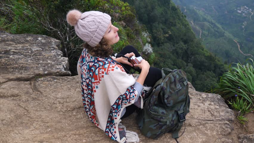 Woman sits on top mountain with camera in hands and looks at majestic landscape. Mountain towers above surrounding world. From height mountain there is breathtaking view traveler strives to capture.