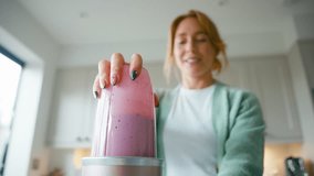 Pull focus shot of woman at home in kitchen making healthy smoothie mixing up yoghurt, banana,raspberries and blueberries in blender- shot in slow motion - Powered by Shutterstock - Get 15% off with code: PIKWIZARD15