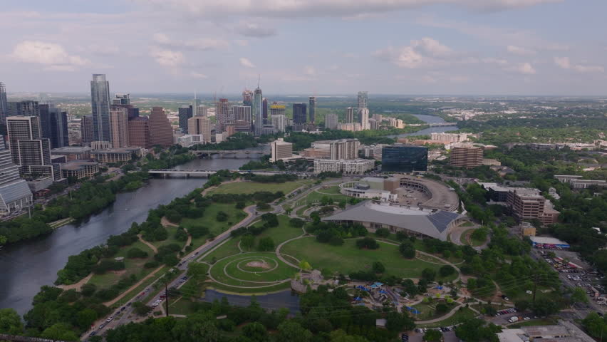 Aerial perspective of vibrant parks in Austin, Texas, with its famous skyline, tranquil Colorado River water against a partly cloudy backdrop