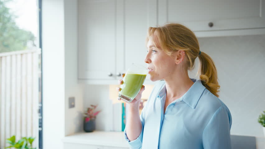 Woman drinking fresh healthy green smoothie made from apples,banana and celery from glass in kitchen at home - shot in slow motion