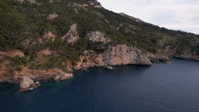 4K Aerial Drone video of a mesmerizing sunset over the sea with an iconic ship and cliffs at Mirador Badia de Pollenca, Mallorca island, Spain