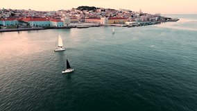 Sailing boats go down the Tagus River past the tourist center of Lisbon, Portugal. Amazing panoramic aerial drone view of an old European city at sunset. High quality 4k stock video
