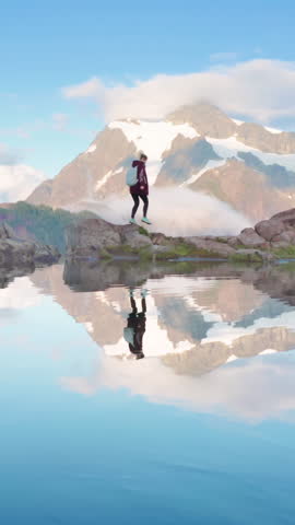 A hiker treks across rocky terrain with a mountain and its reflection in a lake, symbolizing outdoor adventure, nature, hiking, and tranquility in a serene and peaceful setting