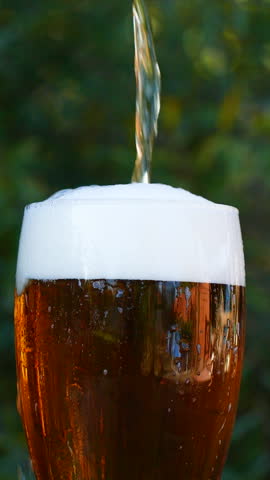 Vertical close-up of pouring beer with foam and bubbles in glass in slow motion
