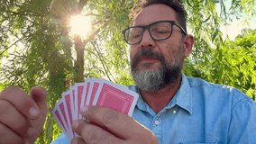 Portrait shot of caucasian adult man sitting at the table outdoors in the park, playing cards game and talking. Outdoor leisure activity playing board table game with friends and having fun enjoying - Powered by Shutterstock - Get 15% off with code: PIKWIZARD15