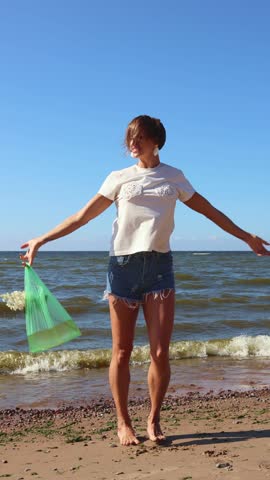 Girl dancins on sunny day. Happy woman jumping on beach on sand in waves of sea with hydrangea flower in bag of water. Vertical video. Taken from hand. High quality 4k footage