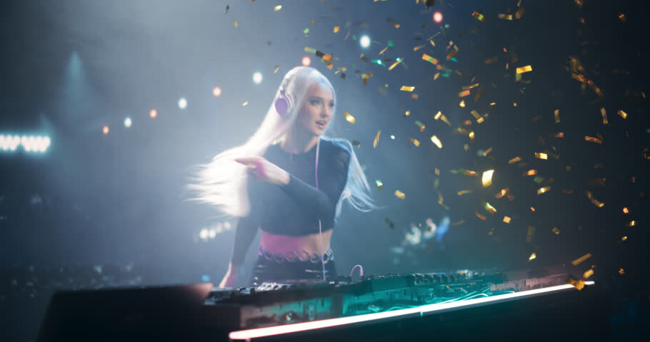 Female Pop Musician in Black Outfit Performing Techno or Trance Music on a Club Stage, Passionately Dancing Behind the Turntables Under Confetti Paper, Creating an Energetic Concert Atmosphere