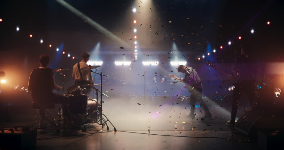 Professional Rock Musicians Performing a Live Set on Festival Stage, Playing Popular Rock Tracks in Front of a Crowded Arena with Falling Confetti. Electrifying Performance at an Indoors Festival