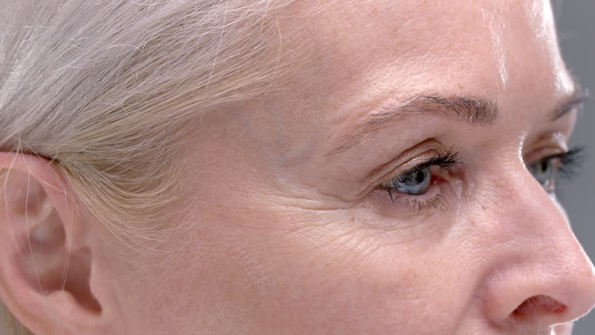 Close-up: eyes of an old woman macro. Senior female smiles and laughs, wrinkles near the eyes. Happy Lady enjoying happy active life, aging. Old skin of wrinkled face of Caucasian. Beauty portrait