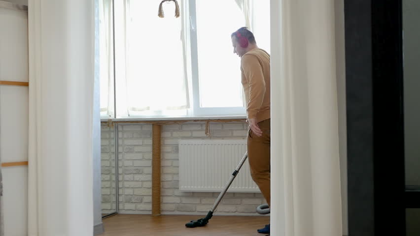 eautiful dance with a vacuum cleaner. House cleaning with dancing. A young man cleans his apartment while listening to music.