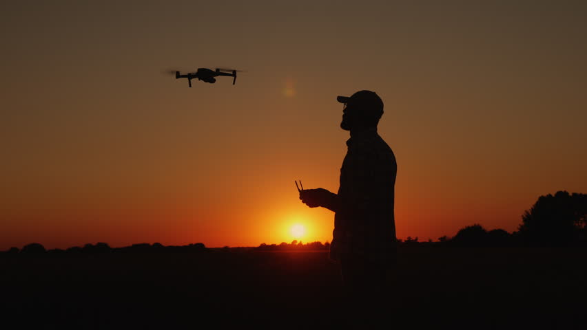 Silhouette a young man lands a drone landing on his hand in nature at sunset