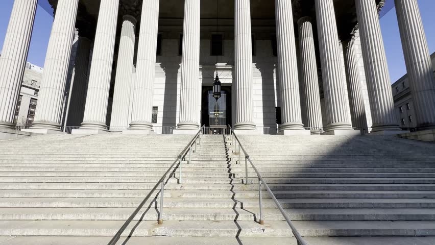 An imposing upward view of the New York County Courthouse, highlighting its grand columns and monumental steps, symbolizing justice and the rule of law in the heart of Manhattan.