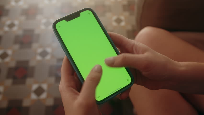 Smart phone with green screen close-up. Fingers of person tapping on screen during game.