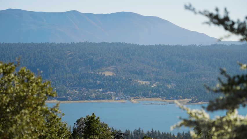A View of Big Bear Lake And Surrounding Mountain Forest Being Seen In Distance Through Brush and Trees, From A Mountain Top