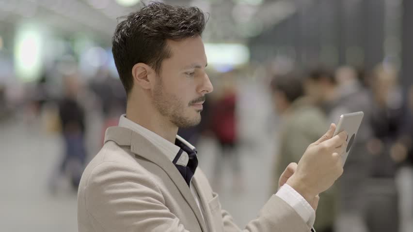 Man is Shown Using a Tablet Screen in the Midst of a Busy Street