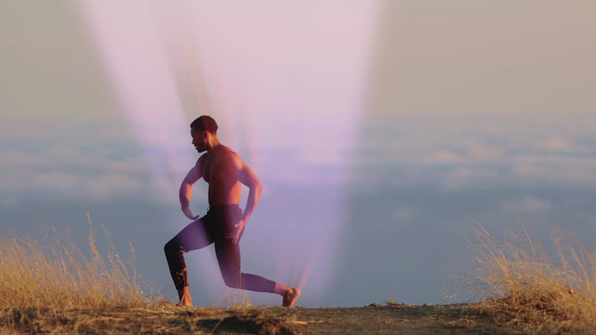 Male ballet dancer doing a choreographic dance move standing on a rock at sunset. Heavenly clouds are in the background and rays of light are coming from his body. 